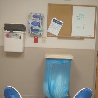 A view of a hospital waiting area with a blue trash can and a bulletin board.