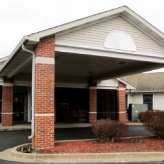 A brick-fronted building with a covered entrance, surrounded by landscaped areas.