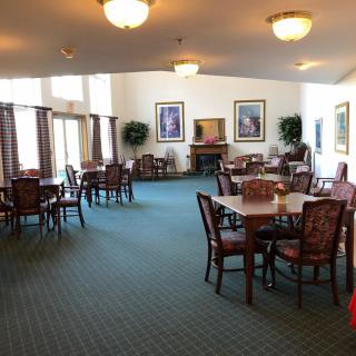 A spacious dining area with neatly arranged tables and chairs, featuring warm lighting and artwork on the walls.
