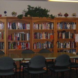A cozy library reading area with bookshelves filled with books and a table surrounded by chairs.