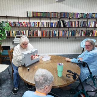 A group of seniors gathered around a table in a library, with one person working on a sewing machine.