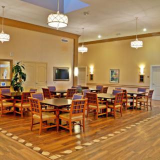 A well-lit dining room with wooden tables and chairs, featuring a polished wooden floor and elegant overhead lighting.
