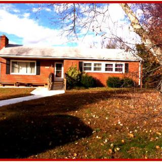 A single-story brick house with a front yard and trees, captured in autumn.