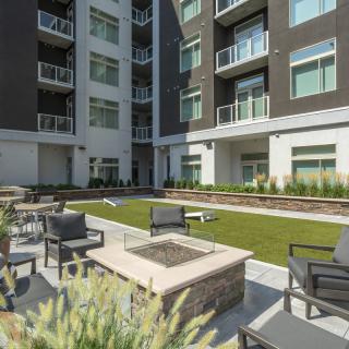 A modern apartment complex features an inviting outdoor seating area with a fire pit and well-maintained landscaping.