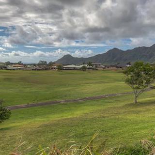 A scenic view of lush green fields with mountains in the background under a cloudy sky.