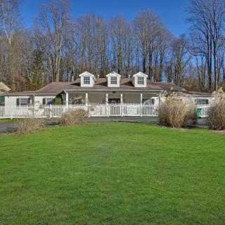 A charming house with a large lawn and trees in the background under a clear blue sky.