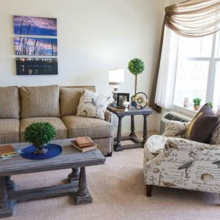A cozy living room featuring a beige sofa, patterned armchair, and wooden coffee table adorned with decorative items and indoor plants.