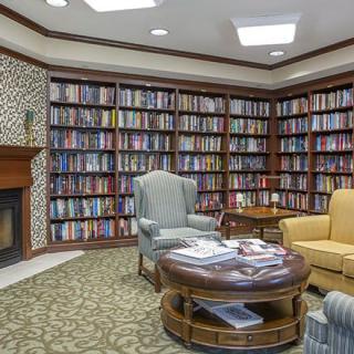 A cozy library corner featuring bookshelves filled with books, comfortable chairs, and a fireplace.