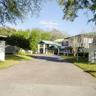 A scenic view of a building with a driveway surrounded by trees under a clear sky.