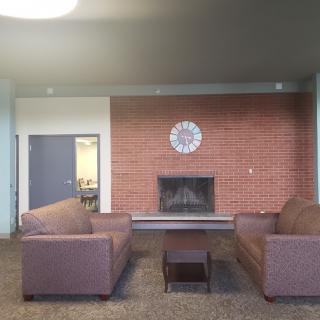 Cozy lounge area with two couches facing a brick fireplace and a clock on the wall.