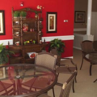 A cozy dining area with a glass table and chairs, featuring a striking red wall adorned with art and a decorative shelf.