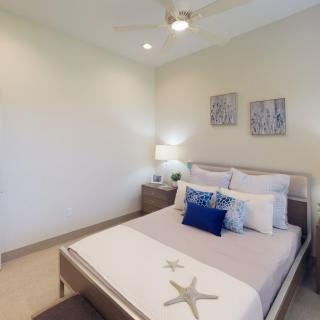 A modern bedroom featuring a neatly made bed with decorative pillows, a nightstand with a lamp, and two pieces of artwork on the wall.
