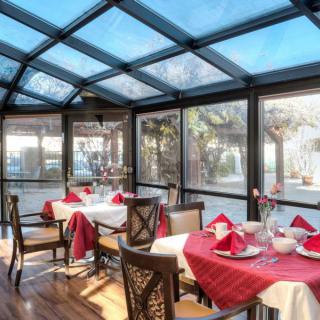 A brightly lit restaurant with elegant table settings under a glass roof.