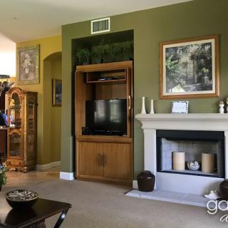 A cozy living room with green walls features a fireplace, a television housed in a wooden cabinet, and various decorative items.