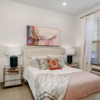 A modern bedroom with a comfortable bed, decorative pillows, abstract artwork above the headboard, and side tables with lamps.