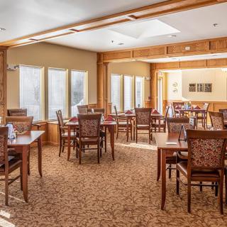 A spacious dining room with wooden tables and chairs, illuminated by natural light.
