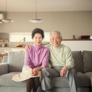 A smiling elderly couple sits together on a sofa in their living room.
