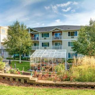 A residential apartment building with a greenhouse and landscaped garden in the foreground.