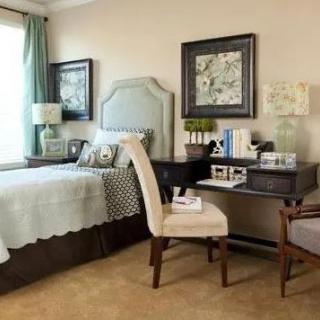 A cozy bedroom with a neatly arranged bed, a small desk with a chair, and wall decorations.