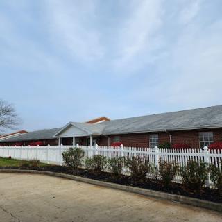 A serene view of a brick building surrounded by a white picket fence against a cloudy sky.
