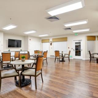 A modern dining area with wood flooring, tables, and chairs, featuring a television on the wall.
