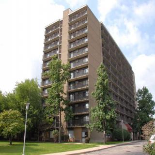 A high-rise apartment building surrounded by trees on a clear day.