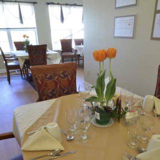 An elegantly set dining table featuring a floral centerpiece with bright natural light streaming in.