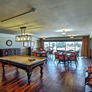 A spacious game room with a billiard table and multiple dining tables, featuring wood flooring and large windows.
