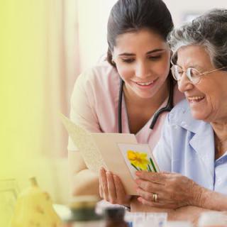 A nurse and an elderly woman smiling while reading a card together.