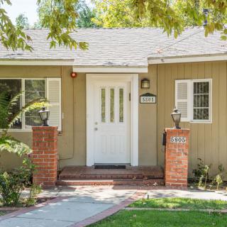 A cozy residential house with a white front door, surrounded by a yard and brick pillars.