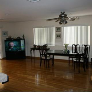 A spacious living room with a dining area, featuring a hardwood floor, dining table, television, and ceiling fan.