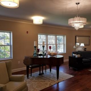 A cozy living room featuring a grand piano, elegant chandeliers, and comfortable seating.
