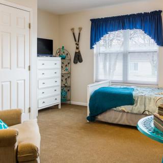 A cozy bedroom featuring a bed with turquoise accents, a white dresser, and a comfortable chair.
