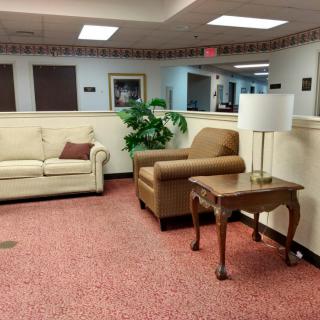 A cozy waiting room with sofas, an armchair, a table, and a lamp.