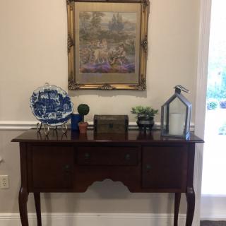 A vintage wooden table with decorative items and a framed painting above it.