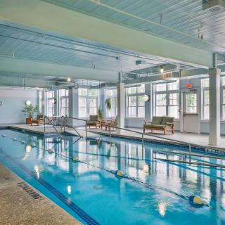 An indoor swimming pool with lounge chairs and large windows.