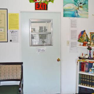 An interior view of an office space with a central door marked by an exit sign, surrounded by various decorations and a bookshelf.