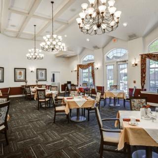 An elegant dining room with chandeliers, neatly arranged tables, and chairs.