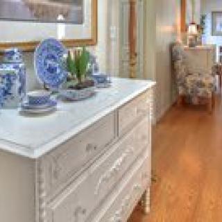 A cozy hallway with a vintage white dresser adorned with blue and white porcelain decor, set against a warm hardwood floor.