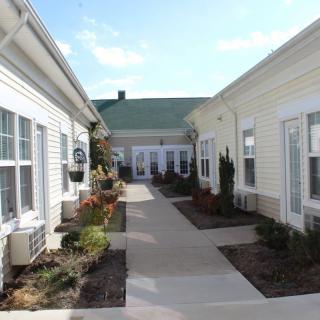 A view of a pathway between two buildings with neatly maintained landscaping and a clear sky above.
