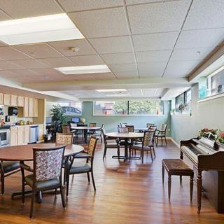 A spacious dining and kitchen area with tables, chairs, and a piano.