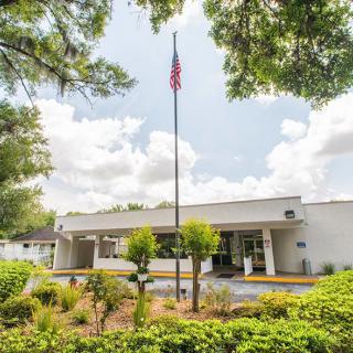 A mid-century modern building with a flagpole in the foreground, surrounded by lush landscaping and under a partly cloudy sky.