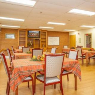 A cozy dining room with neatly arranged tables and chairs, featuring orange tablecloths and a television.