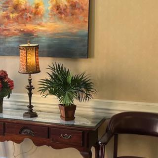 A stylish interior setup featuring a decorative table with a lamp, plants, and a painting on the wall.