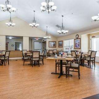 A spacious dining area with wooden floors, tables and chairs arranged neatly under elegant chandeliers.