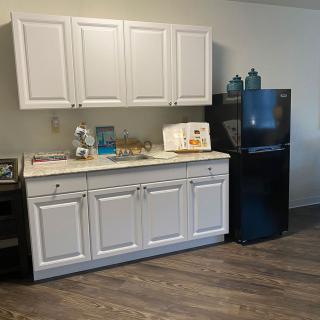 A small kitchen area featuring white cabinets, a countertop with appliances, and a black refrigerator.