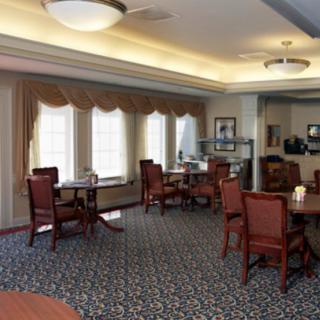 A cozy dining room with multiple tables and chairs, decorated with a patterned carpet and large windows providing natural light.