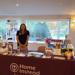 A representative stands at the Home Instead booth, providing information at an event.