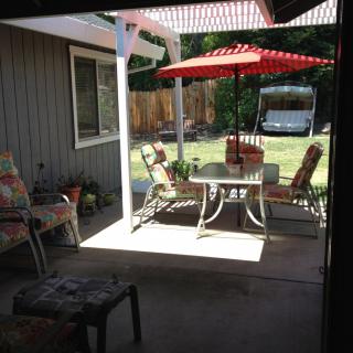 A sunny backyard patio with outdoor furniture and a red umbrella.
