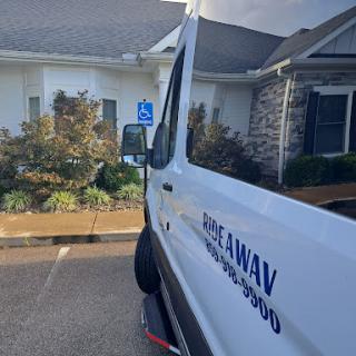 A view of a van parked in a lot, showcasing a handicapped parking sign and the surrounding landscaping.